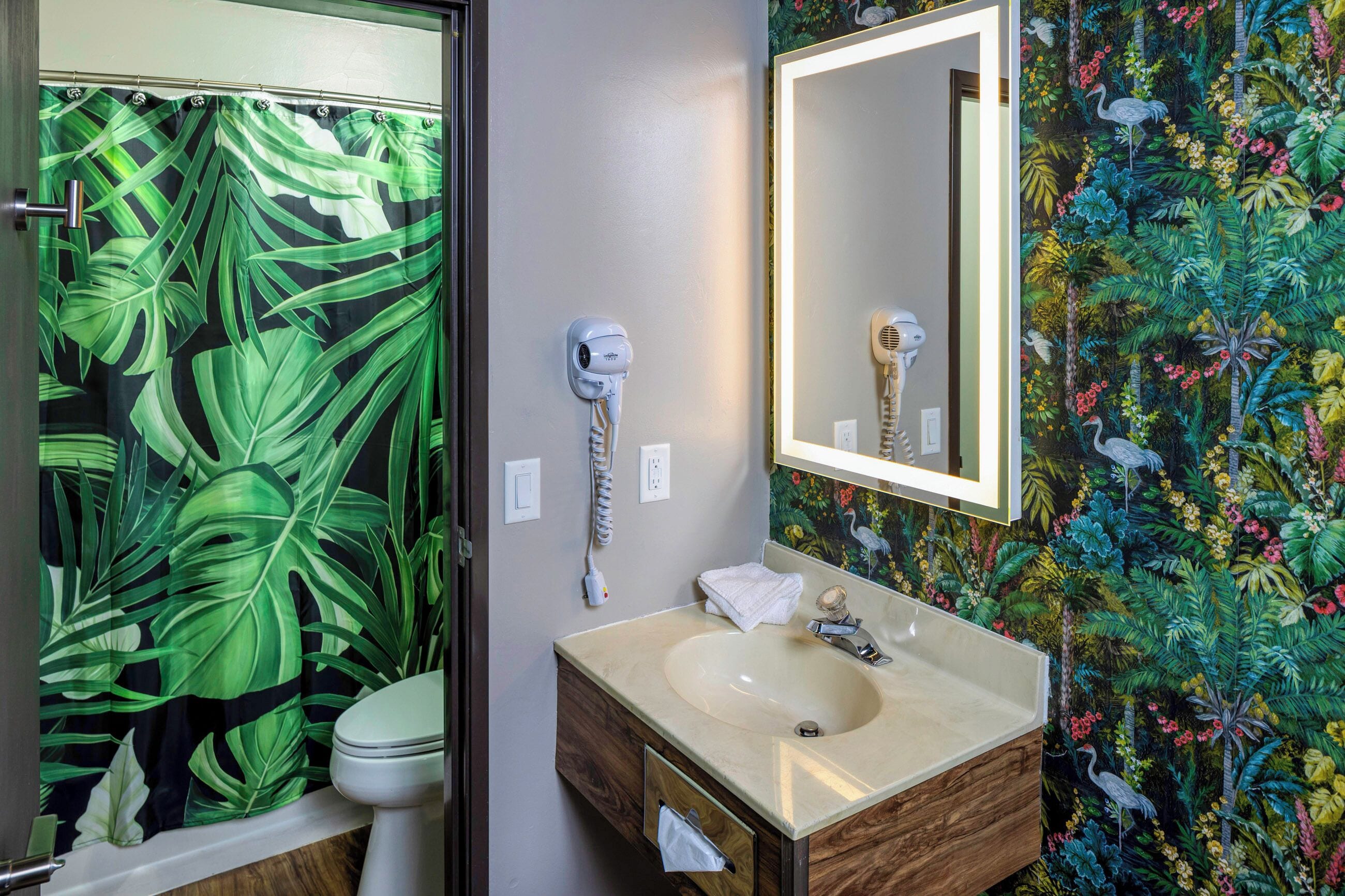A bathroom with a toilet, a sink with a mirror, and a shower curtain with a tropical leaf pattern.