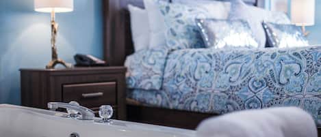 A hotel room with a large bed, a nightstand, a bathroom with a bathtub, and a wall-mounted lamp.