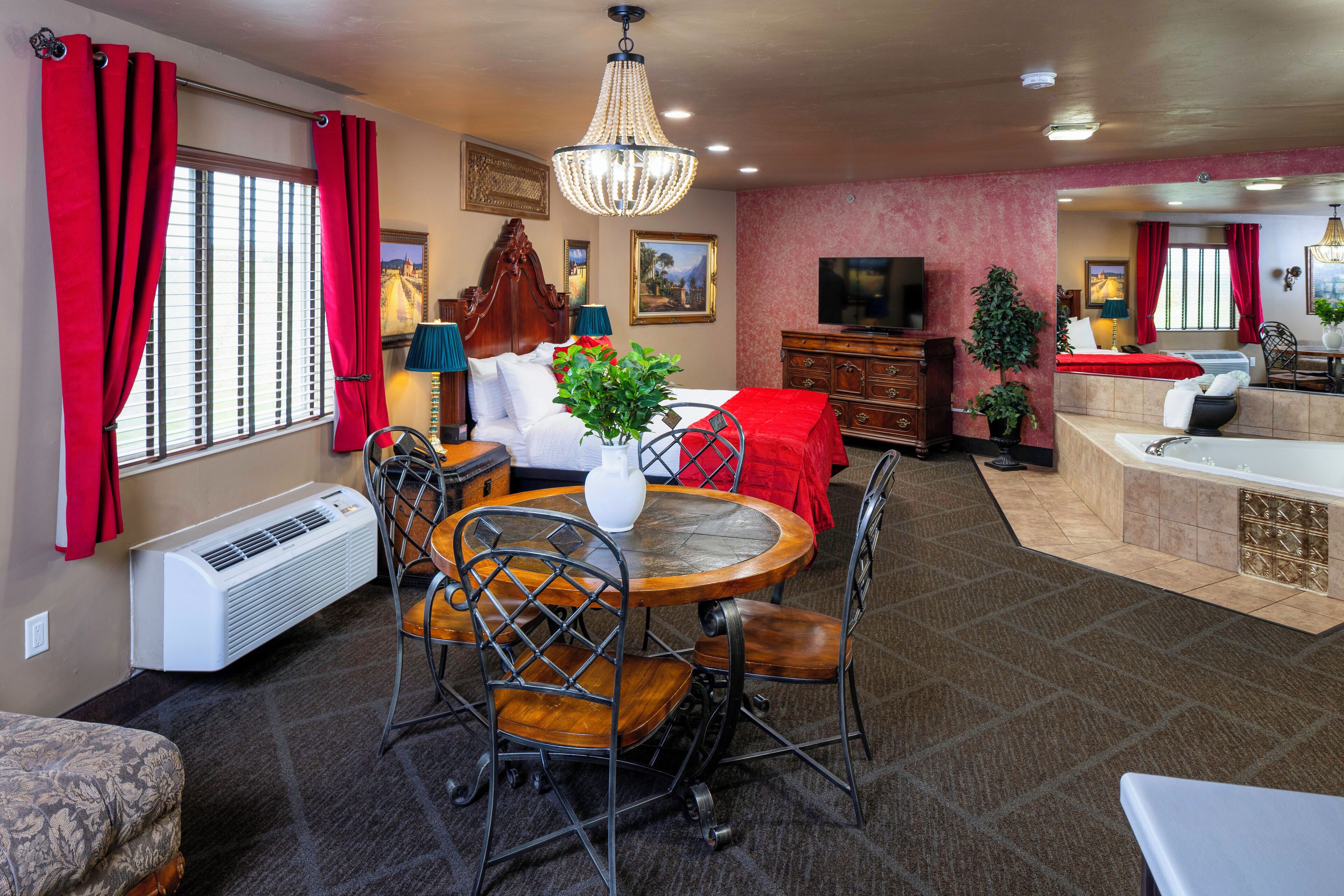 A hotel room with a dining area, a large bed, a television, and a bathroom with a bathtub.