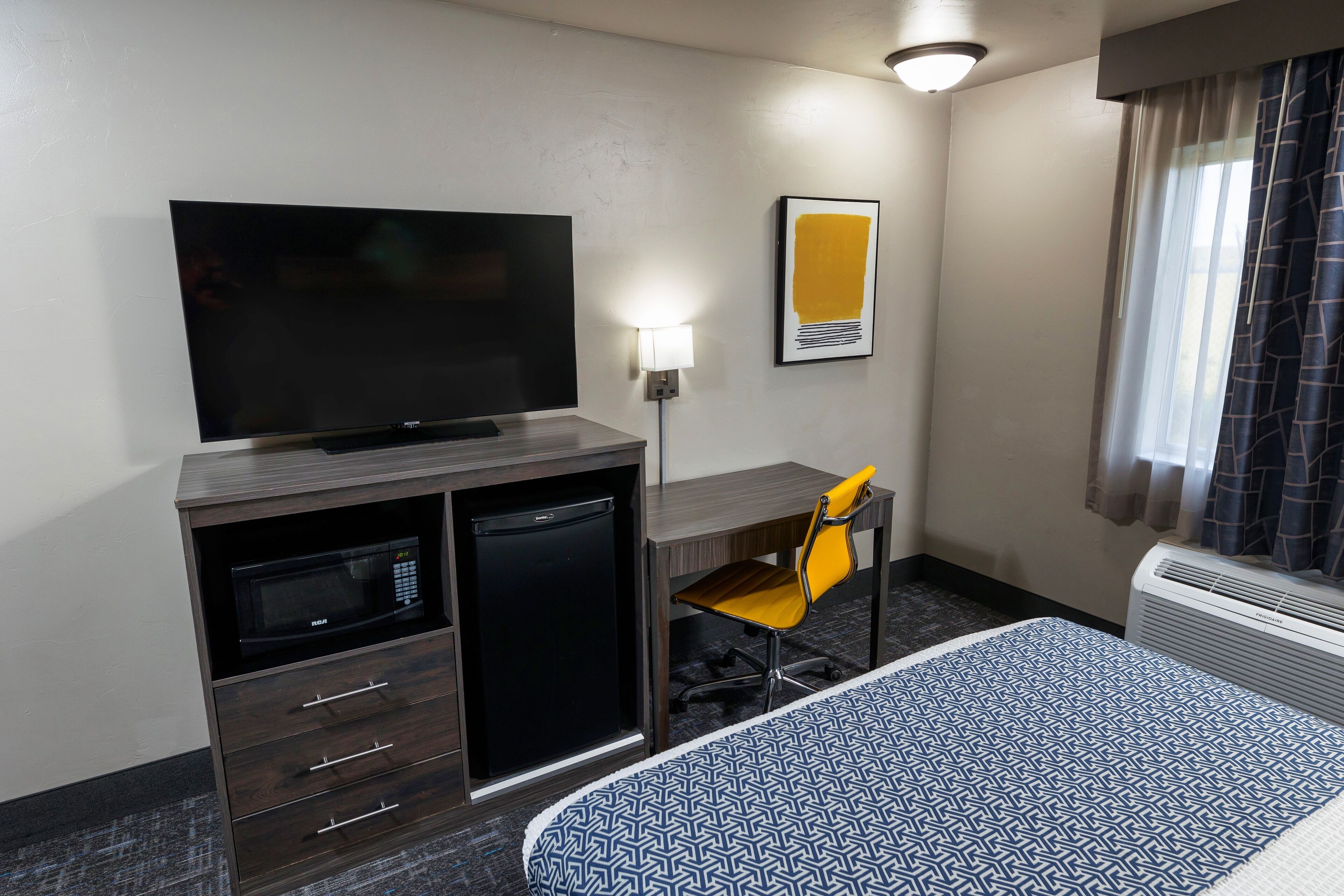 A hotel room with a bed, a desk with a chair, a television, a microwave, and a small refrigerator.