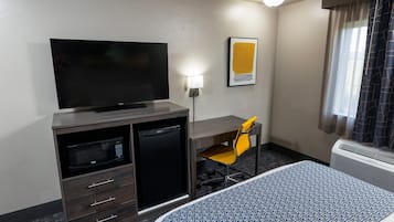 A hotel room with a bed, a desk with a chair, a television, a microwave, and a small refrigerator.