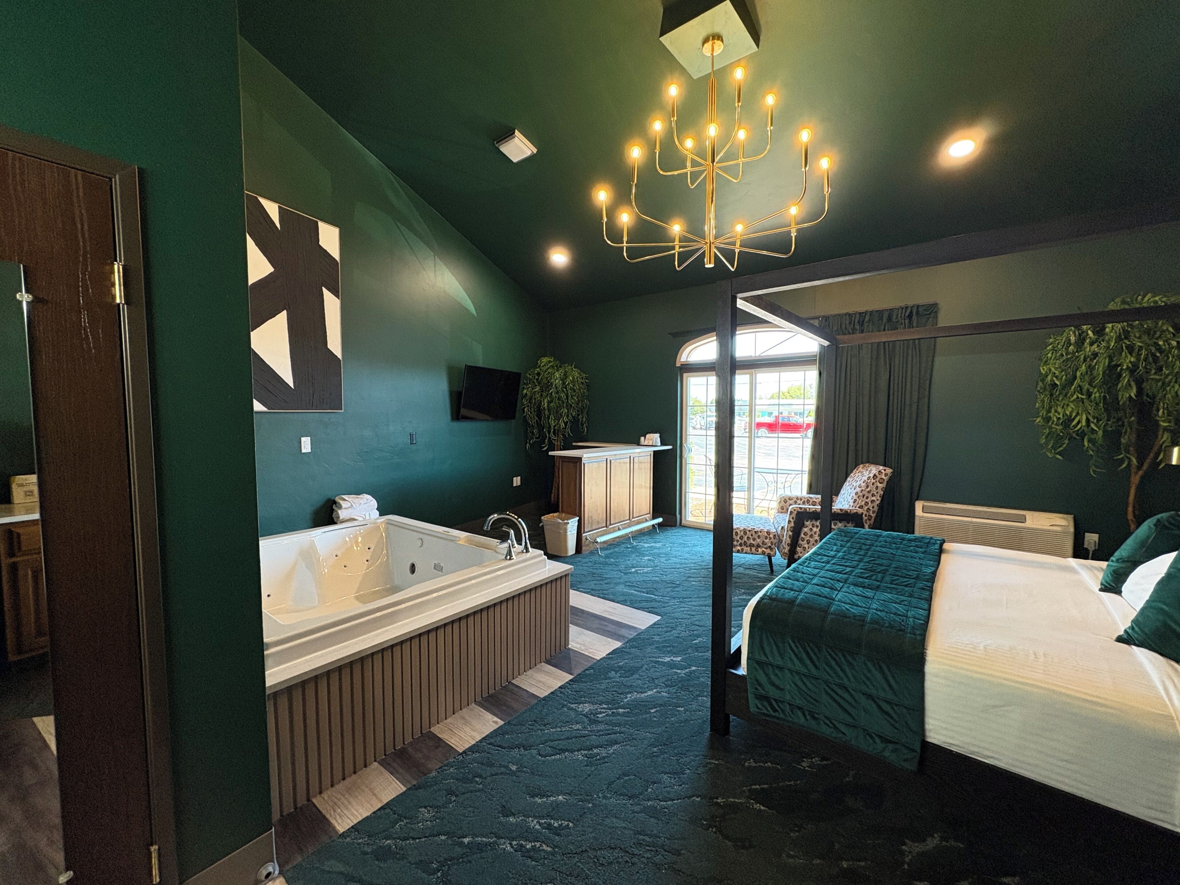 A modern hotel room with a large bed, a separate bathroom with a bathtub, a seating area with a table and chairs, and a view through the window.