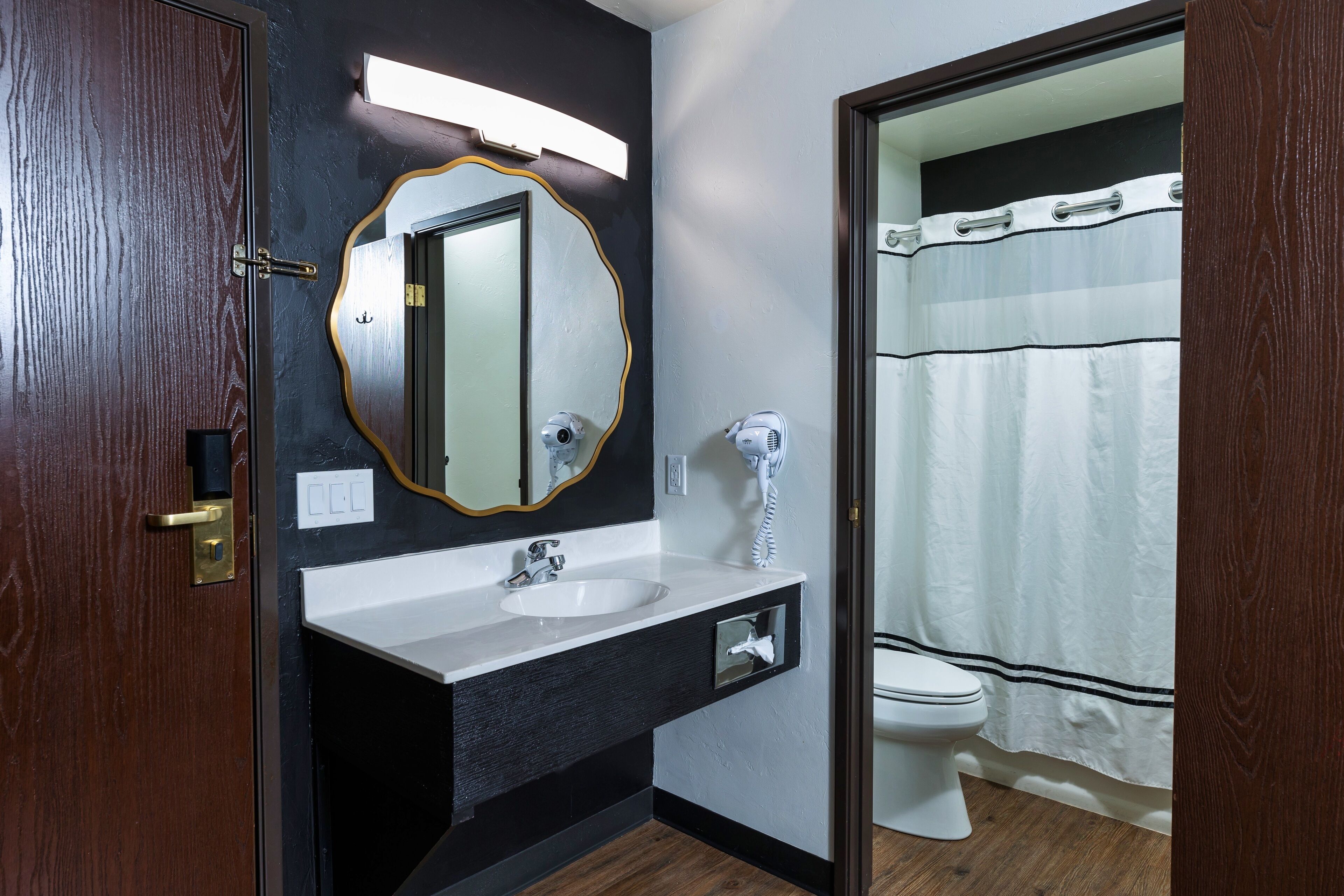 A bathroom with a wooden door, a white sink, a mirror with a gold frame, a toilet, and a shower curtain.