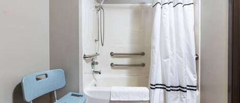 A bathroom with a bathtub, a shower, a white towel, a blue chair, and a handrail.