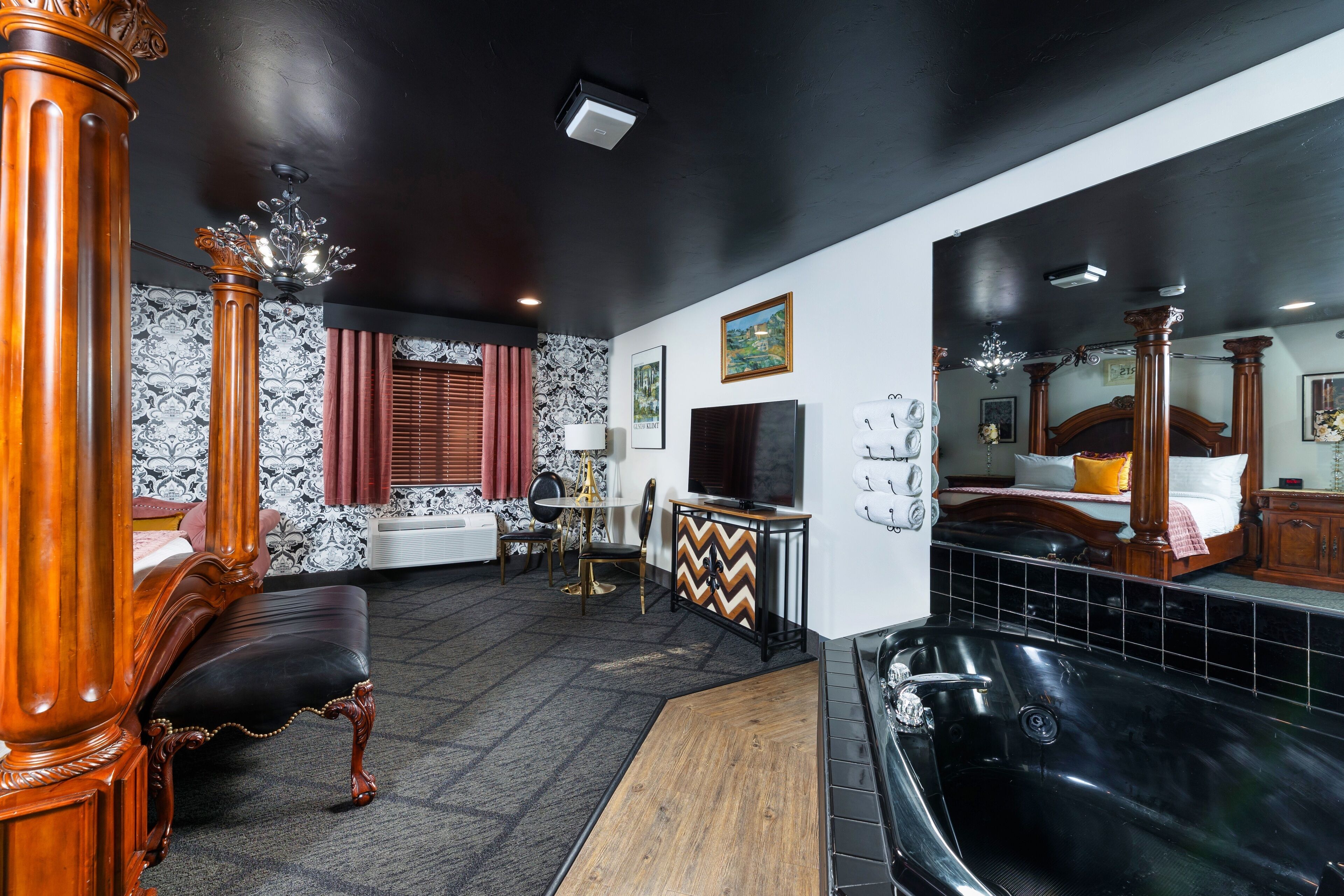 Ein luxuriöses Schlafzimmer mit einem großen Bett, einer Sitzecke mit einem Sessel und einem Tisch, einer Badewanne und einem Fernseher.