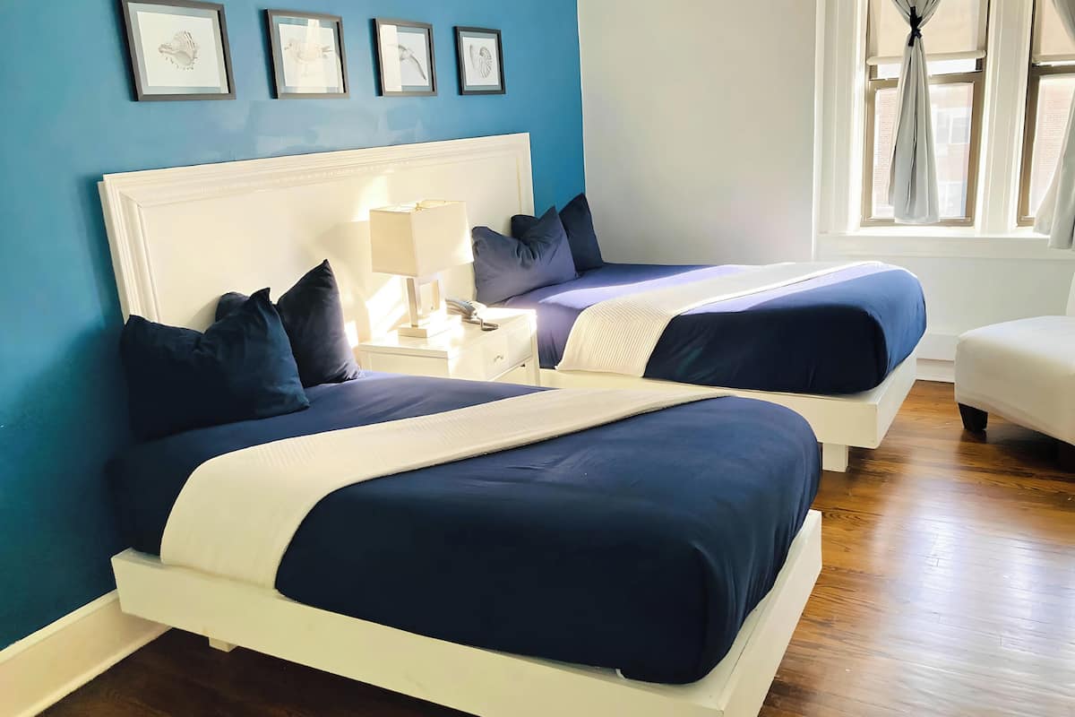 Een hotelkamer met twee bedden, een nachtkastje, een lamp en een raam met gordijnen.