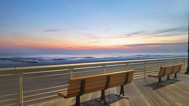A wooden deck with two benches overlooking a beach at sunset.