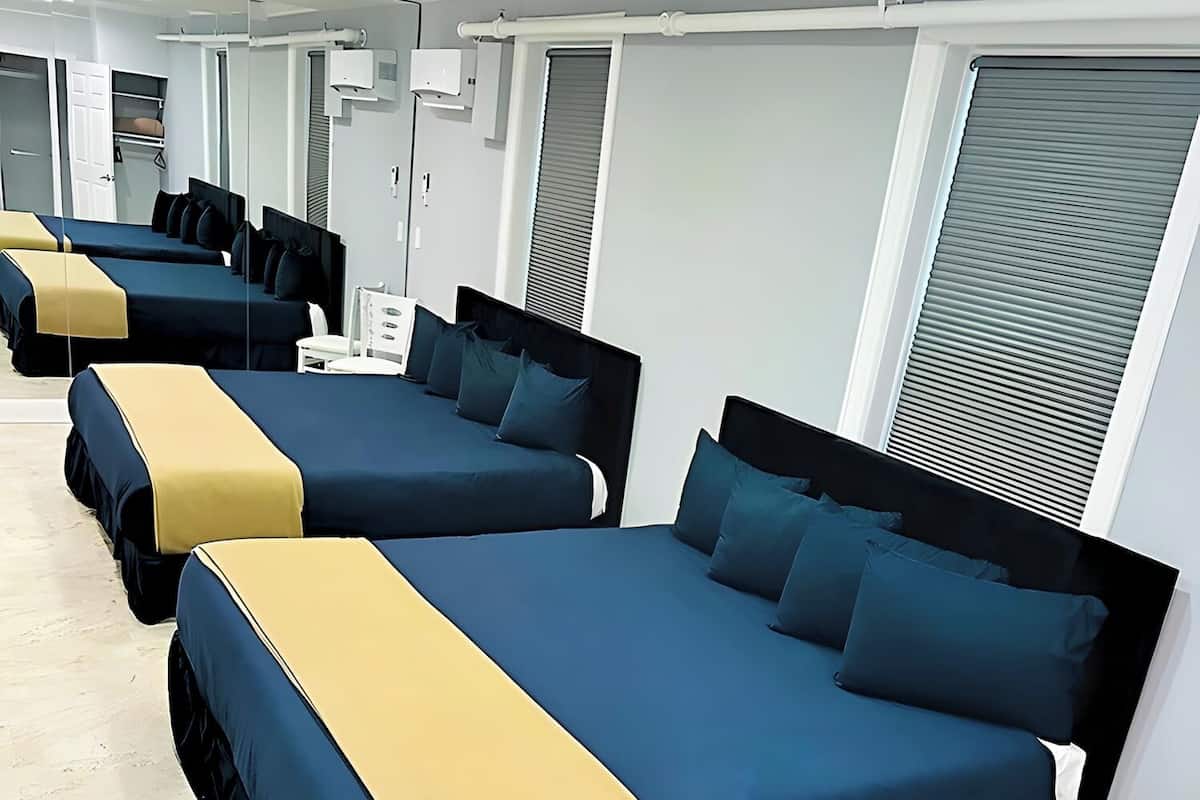 Een hotelkamer met meerdere bedden, elk met een blauwe matras en een geel hoofdeinde.