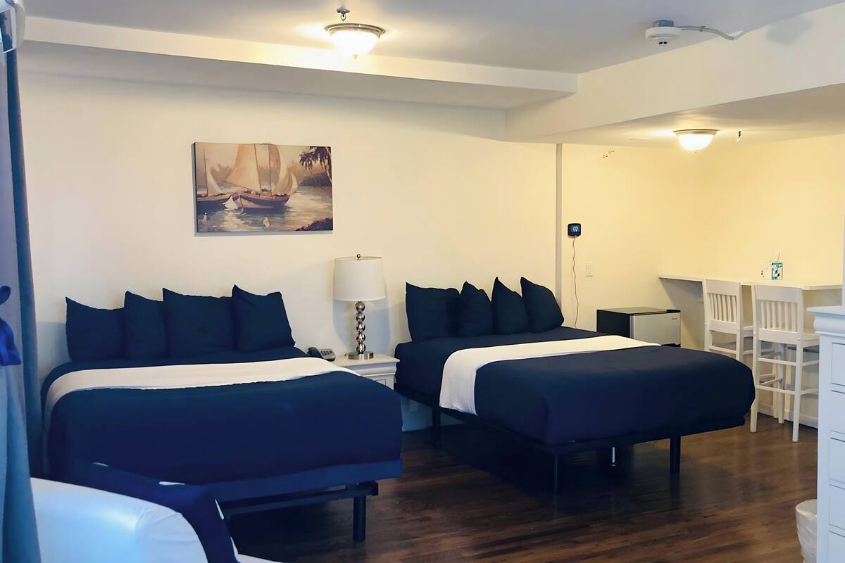 Een hotelkamer met twee bedden, een bureau, een stoel, een dressoir en een schilderij aan de muur.