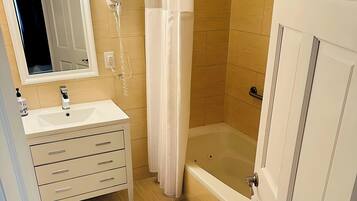 Une salle de bain avec un lavabo blanc, un miroir et un meuble-lavabo, une douche avec un rideau et une baignoire.