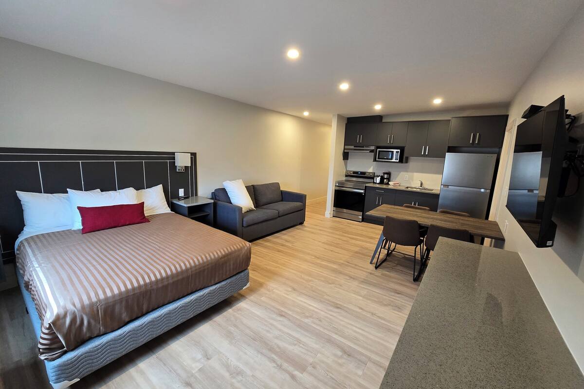 Una habitación de hotel moderna con una cama grande, un sofá, una mesa de comedor y una kitchenette.