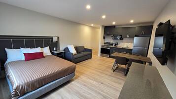 Una habitación de hotel moderna con una cama grande, un sofá, una mesa de comedor y una kitchenette.