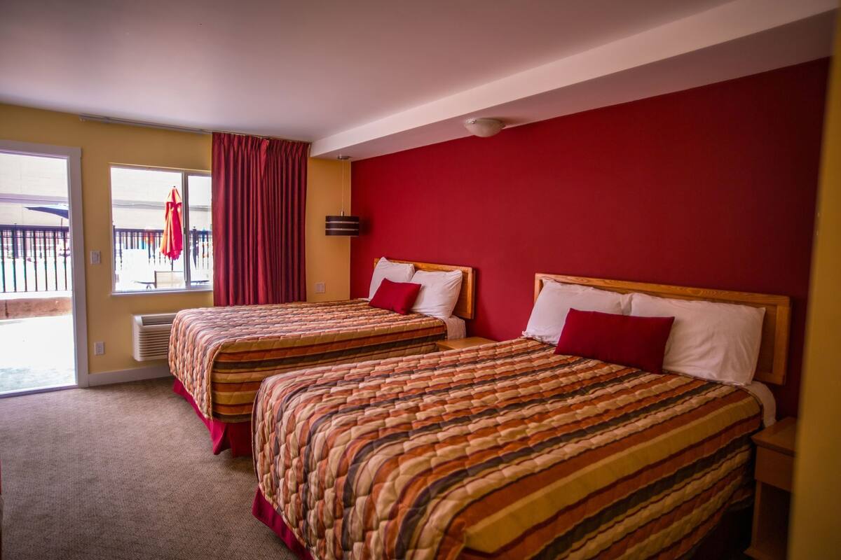 Habitación de hotel con dos camas, una pared roja y vistas al exterior.
