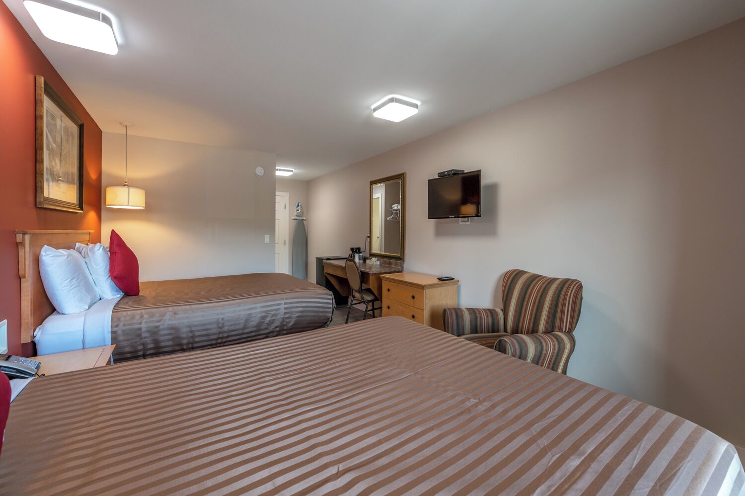 A hotel room with two beds, a desk, a chair, a dresser, and a television.
