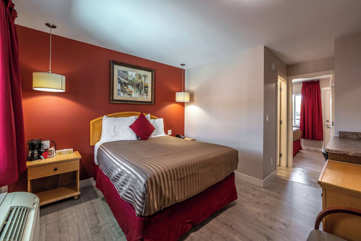 Habitación de hotel con una cama, mesitas de noche, un cuadro y vistas al baño.