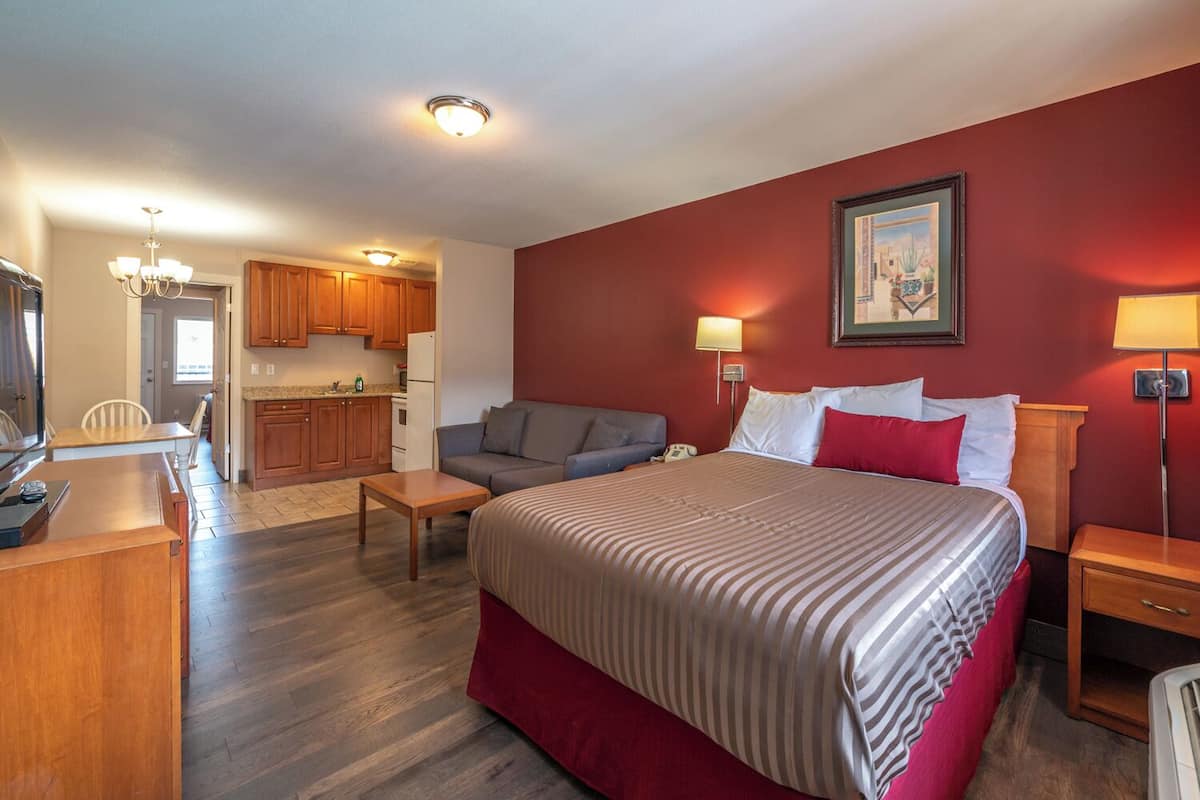 Una habitación de hotel con cama, mesitas de noche, un sofá, un escritorio y una kitchenette.