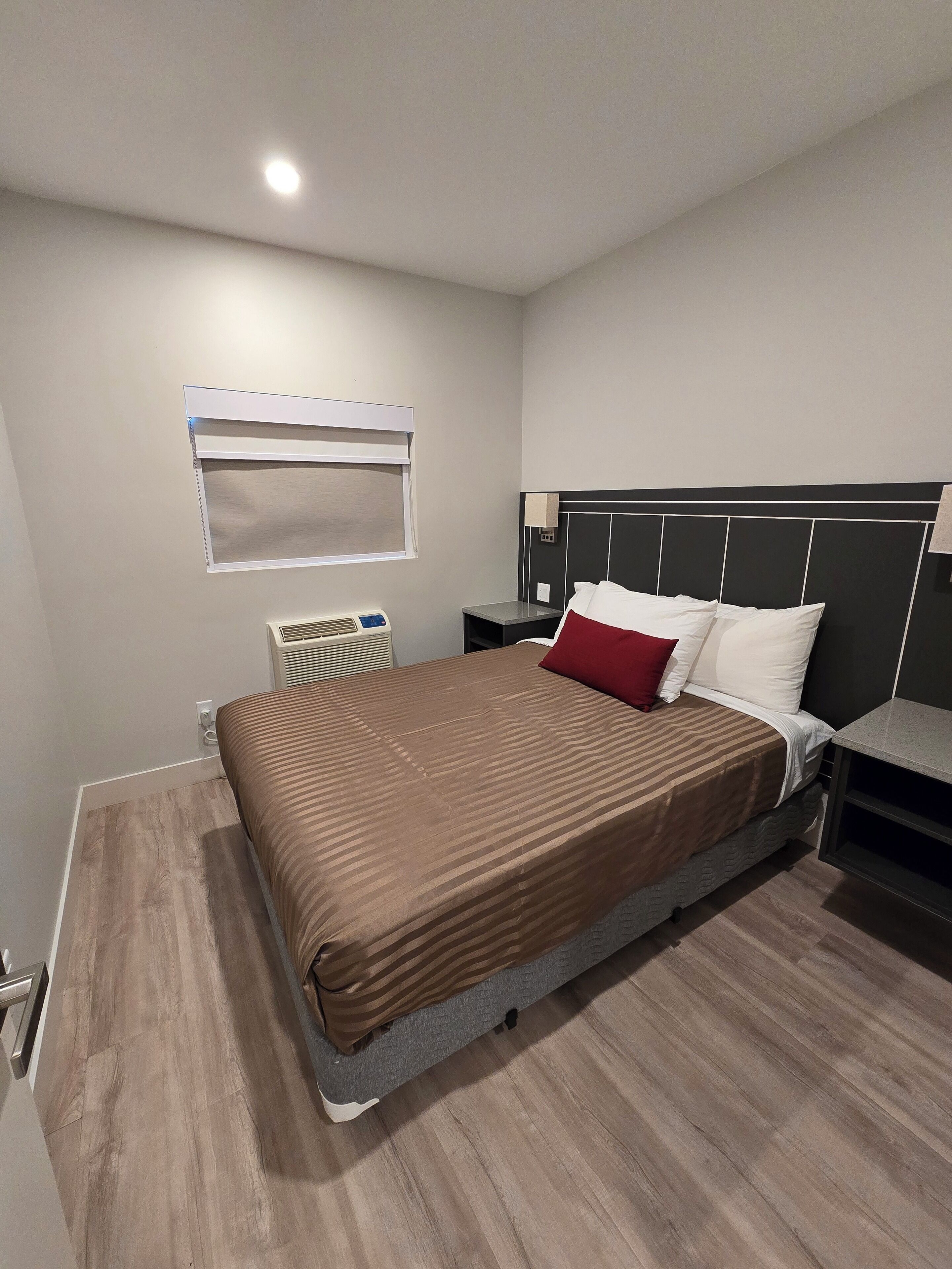 Camera d'albergo moderna con un letto grande, un comodino, un tavolo di fianco al letto, un condizionatore d'aria a parete e una finestra con persiane.