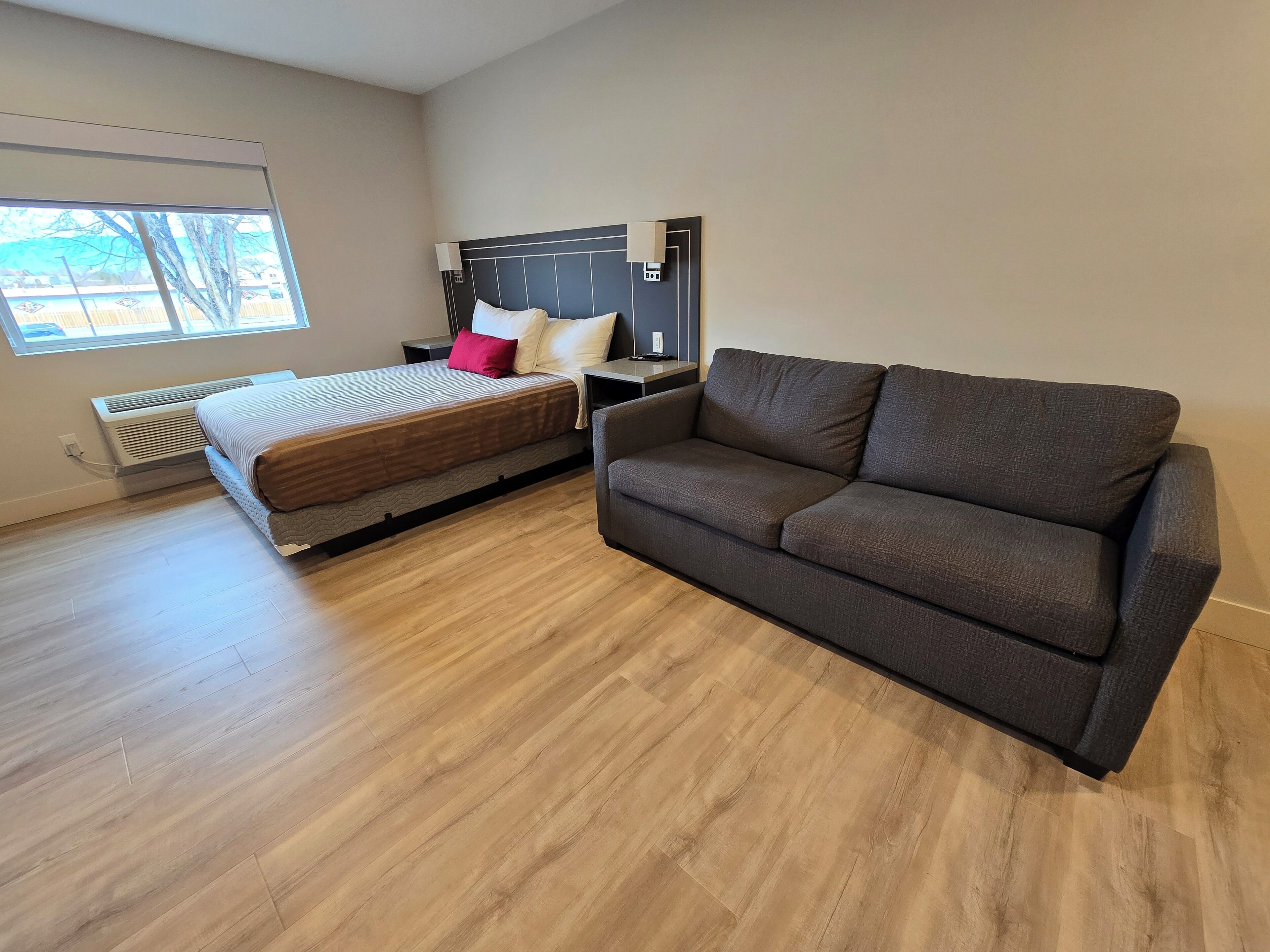 Een hotelkamer met een bed, een grijze bank, een raam en een wandradiator.