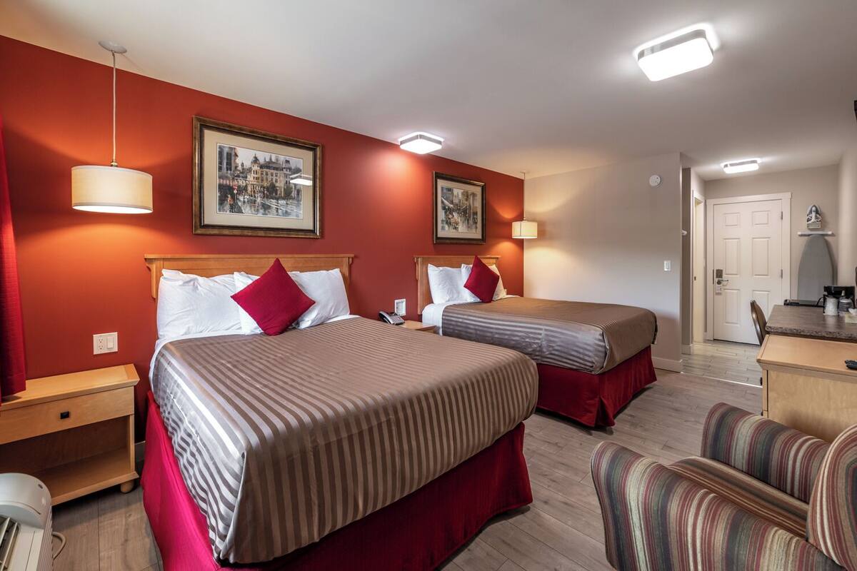 Una habitación de hotel con dos camas, un escritorio, una silla y dos cuadros en la pared.