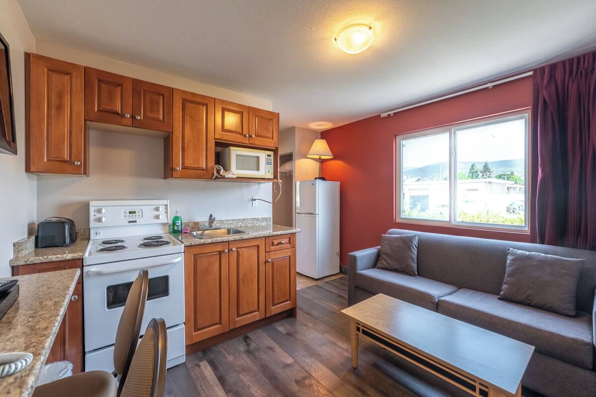 Cocina compacta con armarios de madera, microondas, estufa y refrigerador. Hay un comedor con mesa y sillas, y una sala de estar con sofá y ventana con vistas.