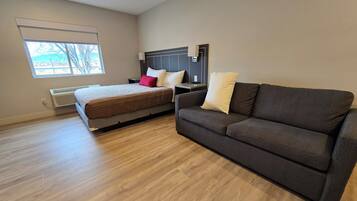A modern hotel room with a bed, a sofa, and a large window.