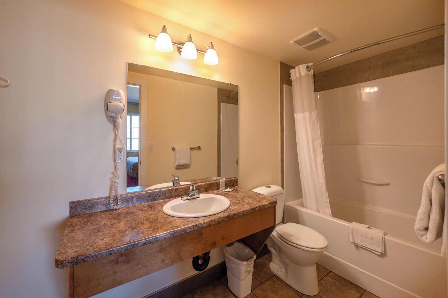 A bathroom with a granite countertop, two sinks, a toilet, and a shower with a curtain.