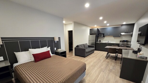 Una habitación de hotel moderna con una cama grande, un sofá, una mesa de comedor y una kitchenette.