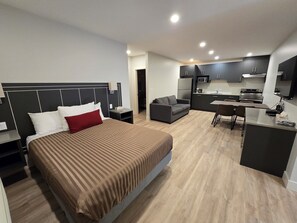 A modern hotel room with a large bed, a sofa, a dining table, and a kitchenette. - Sahara Courtyard Inn Penticton (Penticton)
