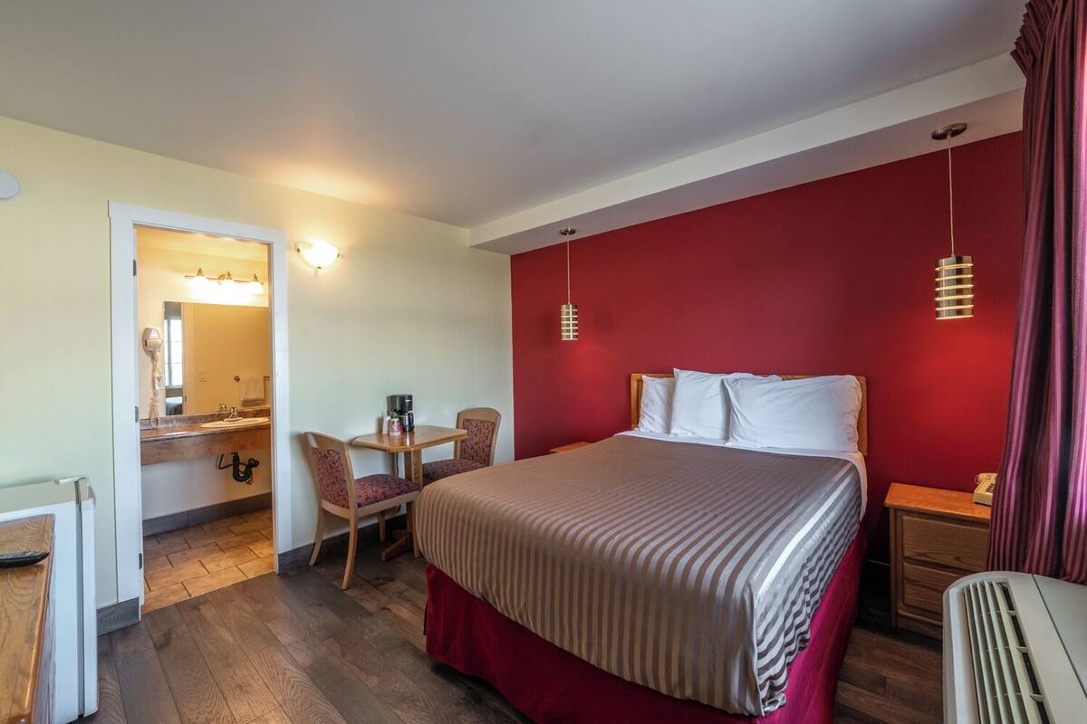Habitación de hotel con cama, escritorio con silla, tocador con espejo y una pared de acento en color rojo.