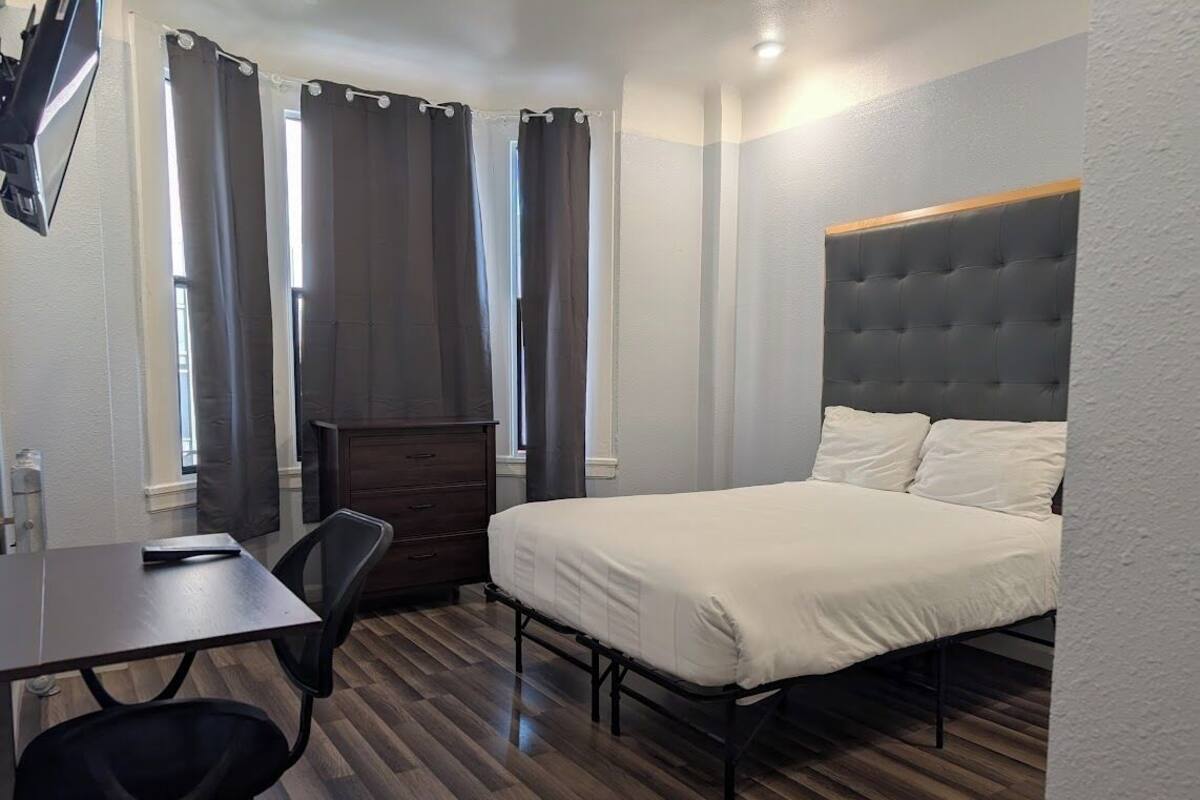 A bedroom with a bed, a desk, a chair, a dresser, and a TV.
