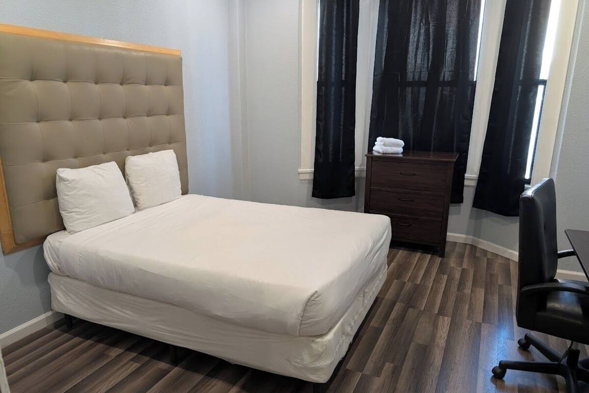 A neatly made bed with a tufted headboard, a wooden nightstand with a lamp, and a black office chair.