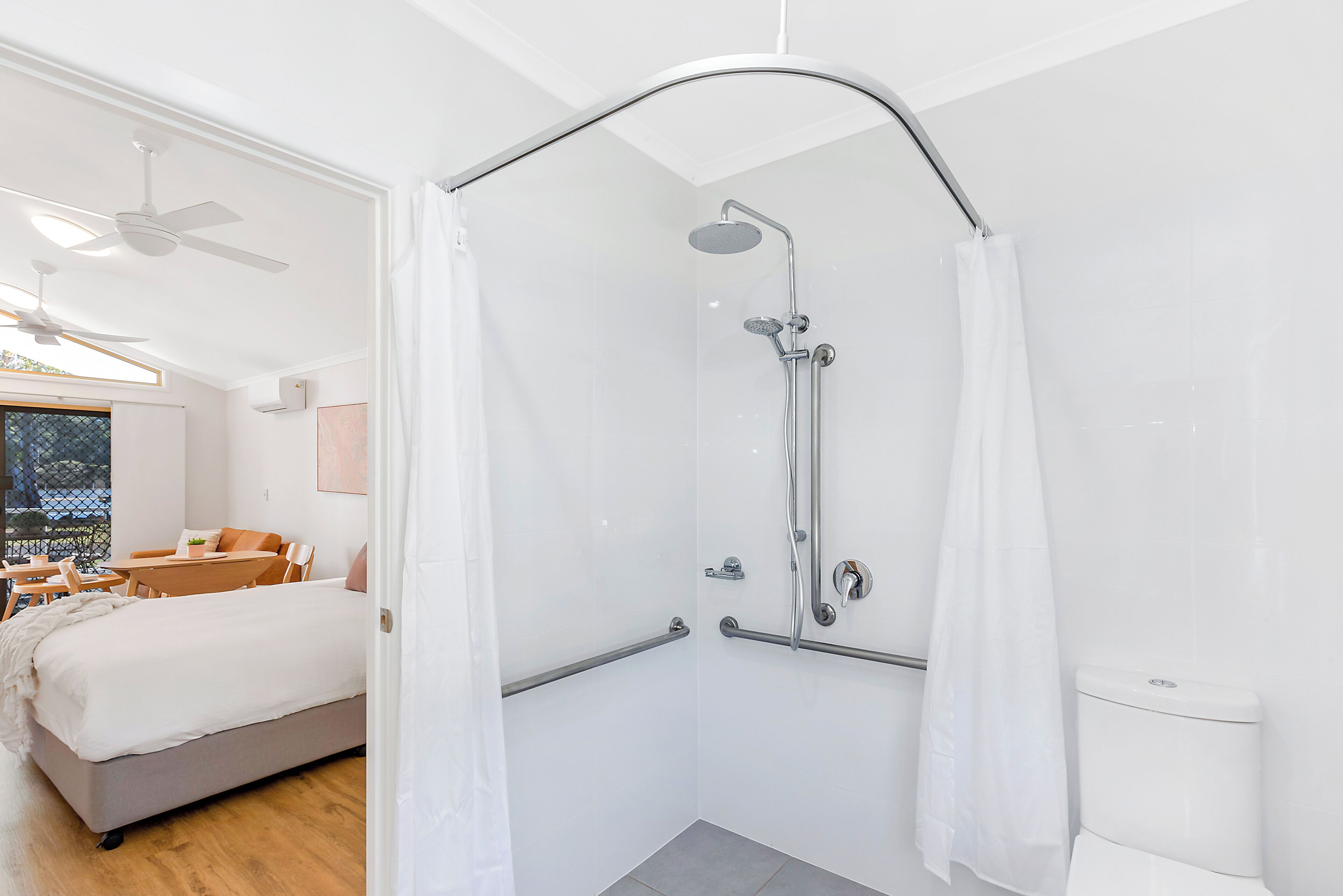 A modern bathroom with a glass shower enclosure, a toilet, and a bed with a view of the outdoors.