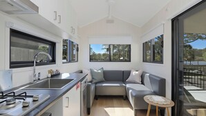 A compact kitchen with a gas stove, sink, and modern appliances. A gray sofa and a small wooden table are positioned near a large sliding glass door that opens to a balcony.