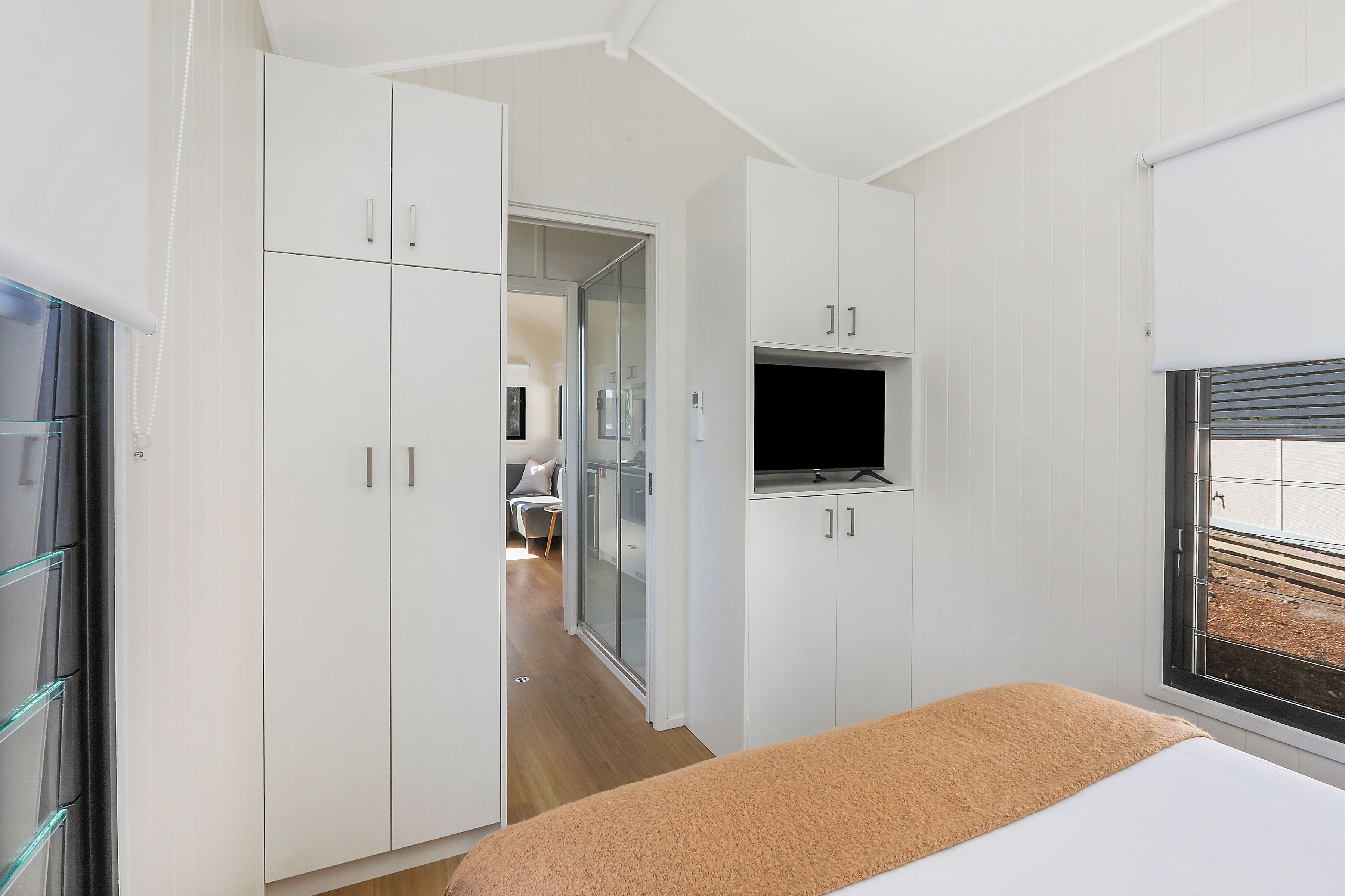 Un dormitorio con cama, televisión montada en la pared y ventana con persianas.