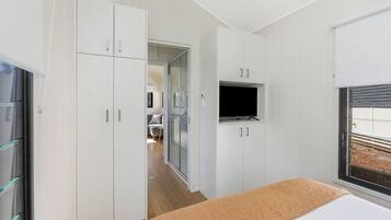 Un dormitorio con cama, televisión montada en la pared y ventana con persianas.