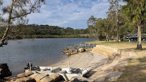A lakeside area with boats docked, a sandy beach, and a stone barrier.