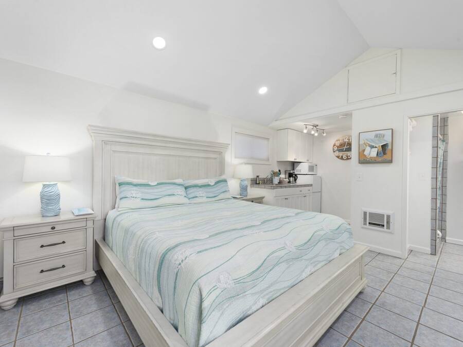 Un dormitorio con cama, mesitas de noche, cómoda, kitchenette y baño.
