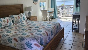 A bedroom with a bed, a nightstand, a chair, a table, and a view of the sea. - Bodega Harbor Inn (Bodega Bay)