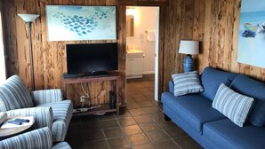 A cozy living room with a wooden interior, a flat-screen TV, striped sofas, and a tiled floor. - Bodega Harbor Inn (Bodega Bay)