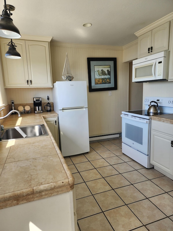 A kitchen with white cabinets, a white refrigerator, a microwave, an oven, a kettle, and a coffee maker.