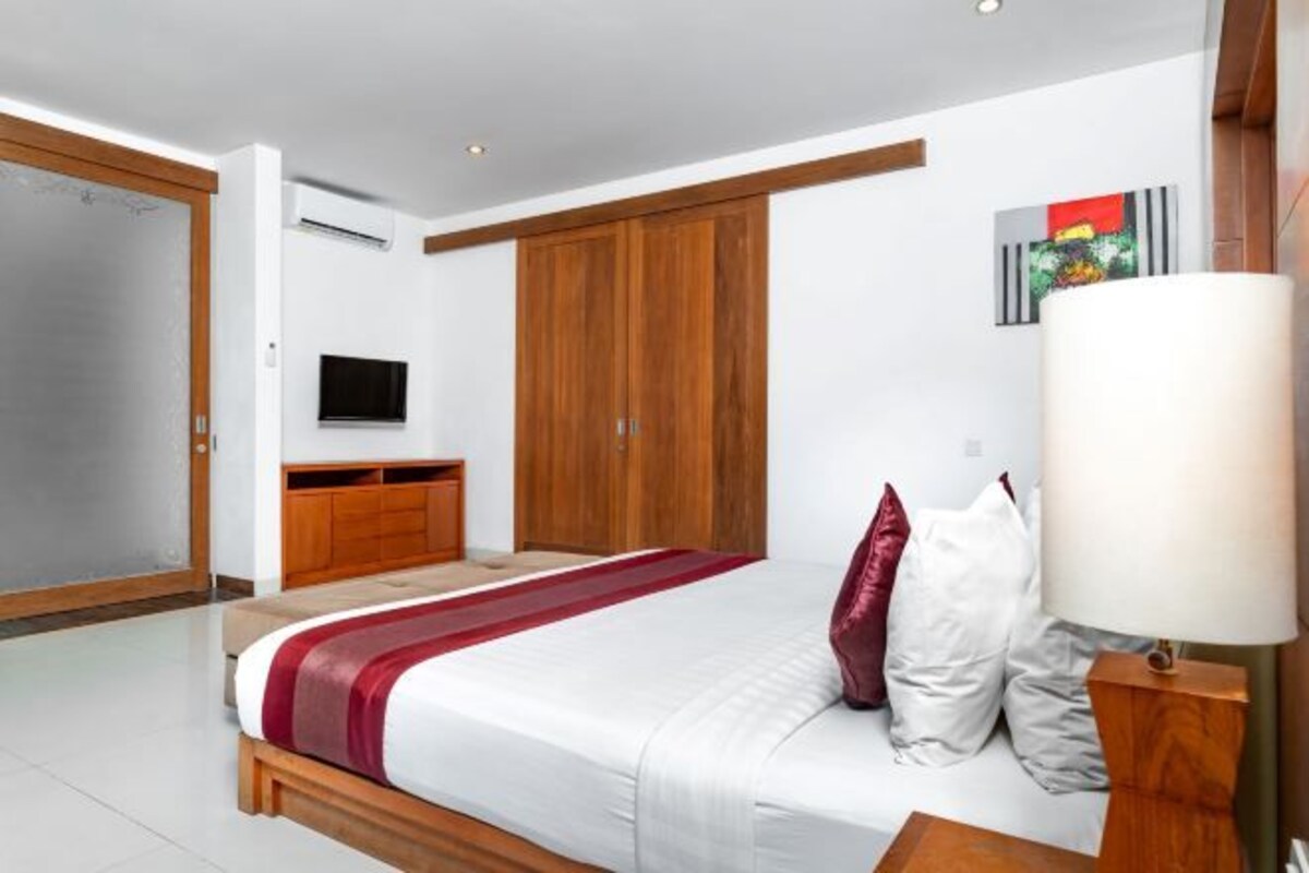 A bedroom with a bed, a TV, a wardrobe, and a painting on the wall.
