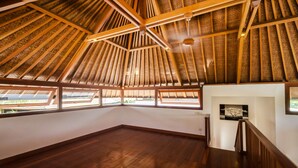Una habitación amplia con techo alto inclinado y vigas de madera. Cuenta con ventanas grandes a lo largo de una pared, que dejan entrar luz natural.