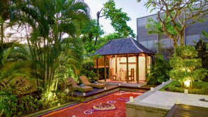 Un resort tropical con una zona de estar cubierta, un sendero adornado con flores y abundante vegetación.