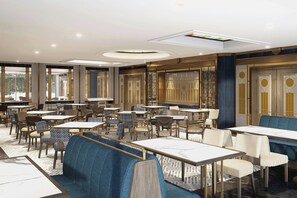 Ein geräumiges Restaurant mit verschiedenen Sitzbereichen, darunter Essecken und Tische, und einem modernen Deckenstil.