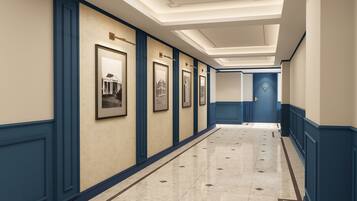 A hotel corridor with framed pictures on the walls, a tiled floor, and a blue door at the end.
