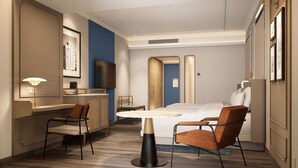 A hotel room with a bed, two chairs, a small table, a TV, and a lamp. - Grand Hotel Preanger, Bandung, a Tribute Portfolio Hotel (Bandung)