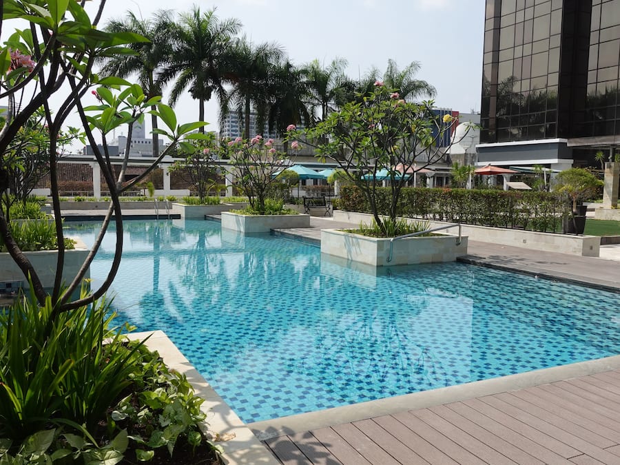 A swimming pool with a checkered pattern, surrounded by greenery and modern buildings.