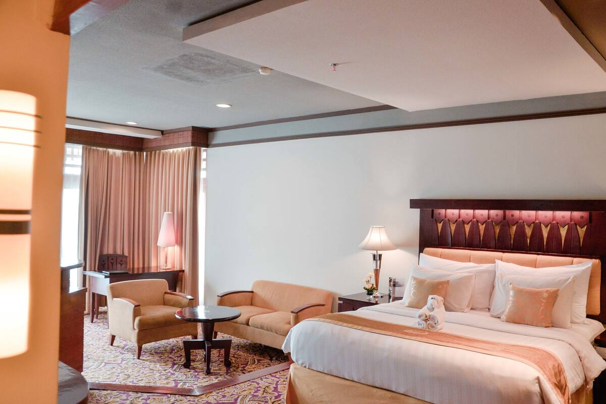A hotel room with a large bed, a sofa, a small table, and a desk.