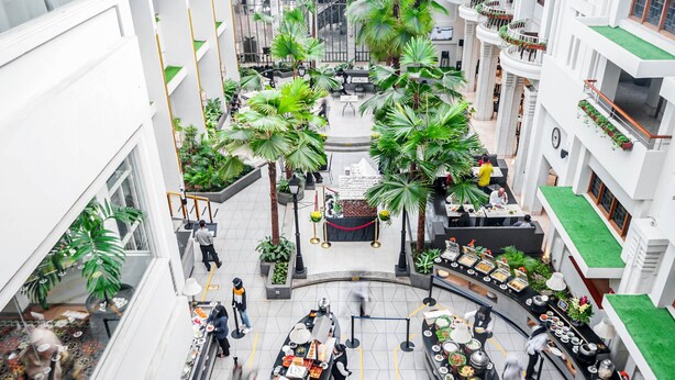 A multi-level atrium with a central open area surrounded by seating, palm trees, and a buffet setup. - Hotel Savoy Homann (Bandung)