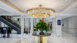 A spacious lobby with a grand chandelier, a piano, and a central plant on a round table. - Hotel Savoy Homann (Bandung)